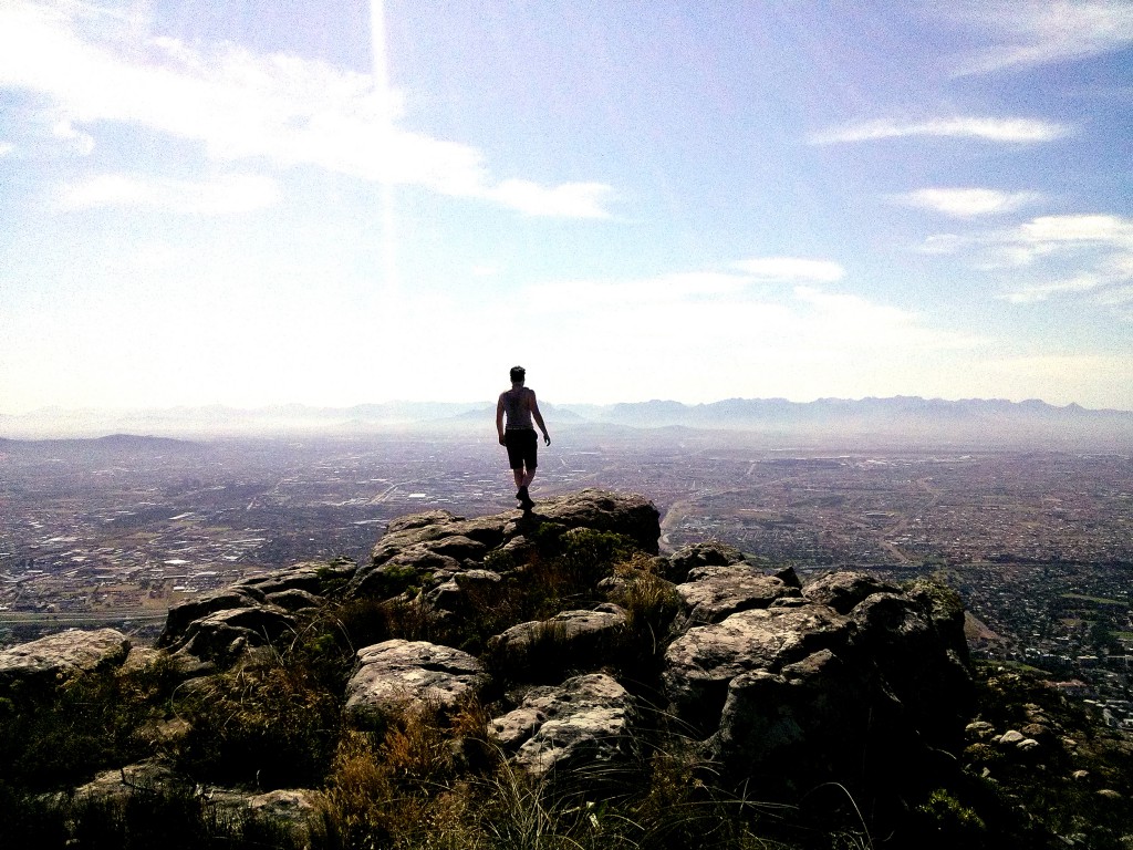 Man standing ontop of a mountain looking towards a city